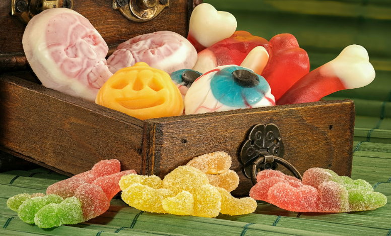 A wooden box brimming with assorted Halloween themed candies and gummy bears, not safe for pet consumption.