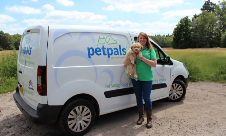 A white Petpals pet care van with Pet Carer holding a white dog ahead of a walk in the park.